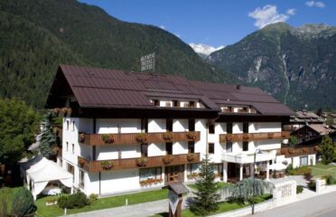 The Dolomites Passover Program in Pinzolo, Italy - - Kosher Vacations in Italy - Tourman - Charming Alpine hotel surrounded by mountains, offering cozy accommodations and scenic views, ideal for guests seeking a peaceful retreat in nature.